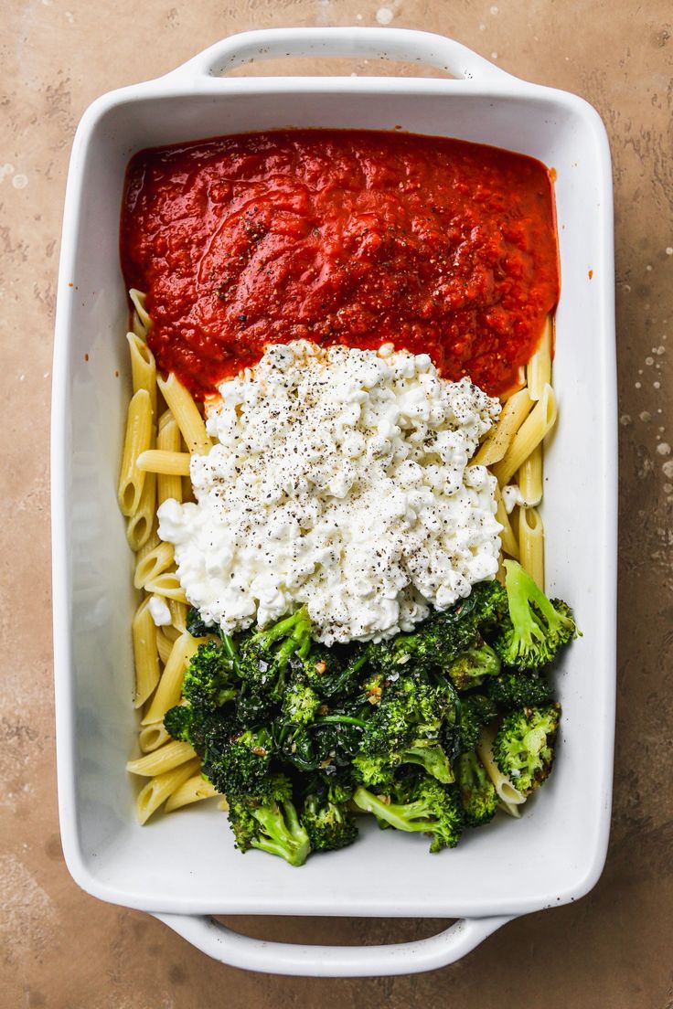 a white dish filled with pasta, broccoli and sauce