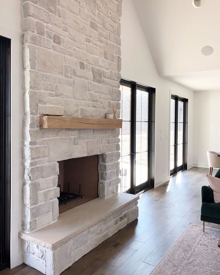 a living room with a stone fireplace and large windows in the back wall, along with an area rug on the floor