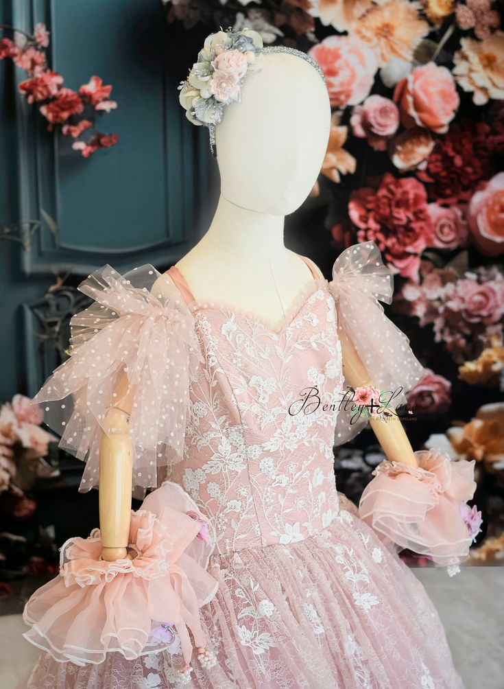 a pink dress with flowers on the head and sleeves is displayed in front of a floral wall