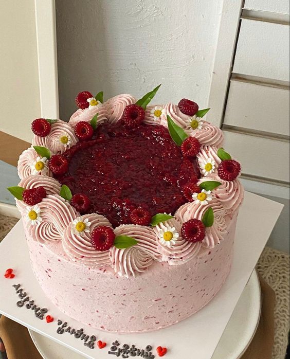 a cake with pink frosting and raspberry toppings on a white plate