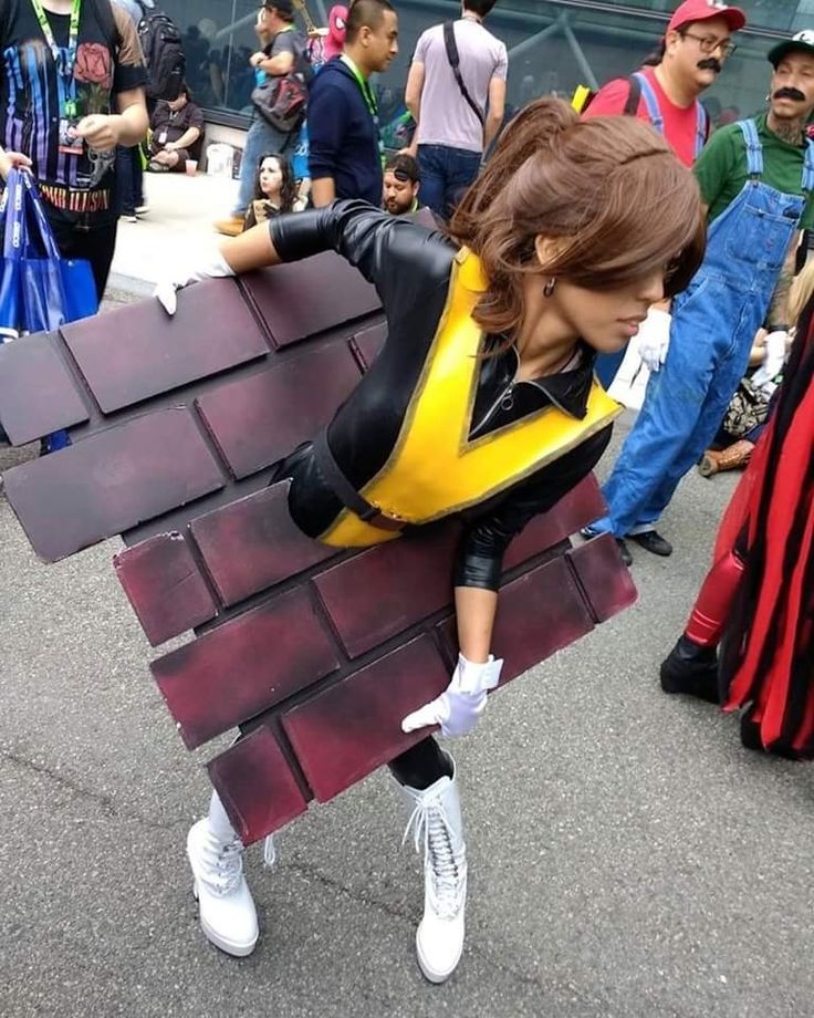 a woman dressed in black and yellow is leaning on a brick wall with other people around her