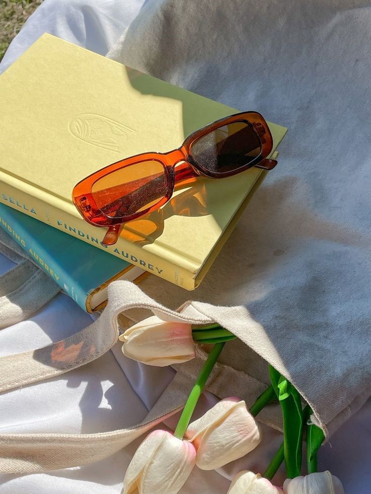 a pair of sunglasses sitting on top of a book next to tulips and flowers