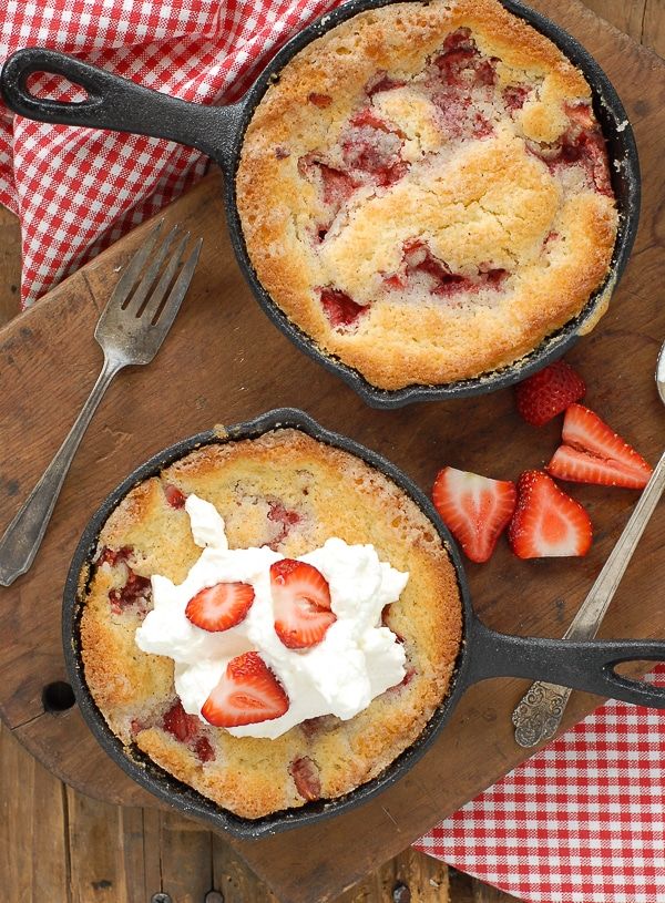 two pies with strawberries and whipped cream in them on a cutting board next to utensils