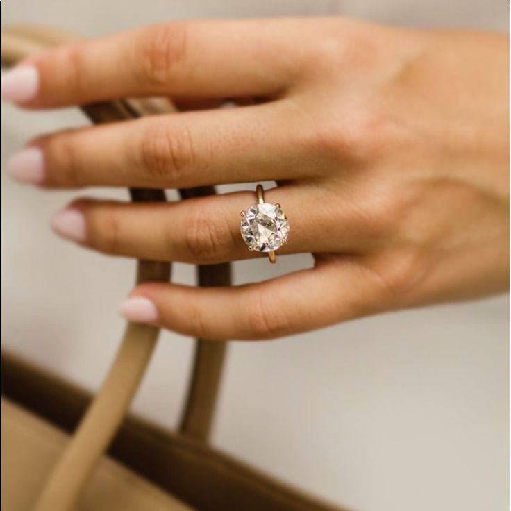 a woman's hand with a diamond ring on her finger and purse in the background