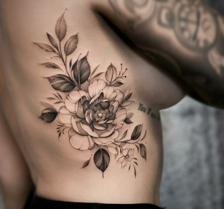 a woman's stomach with flowers and leaves on her side, which is covered in tattoos