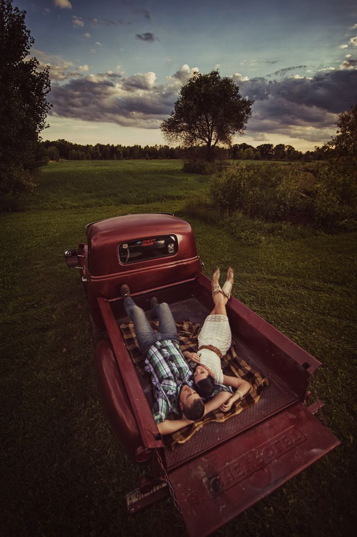 two people laying in the back of a red pickup truck with an open bed on it