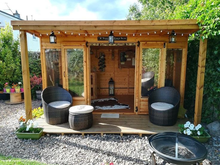 a small wooden shed with two wicker chairs and a fire pit in the middle