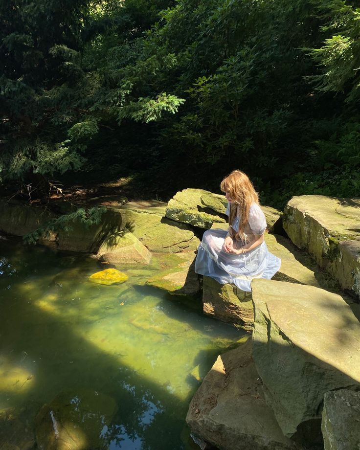 a woman sitting on top of a rock next to a small pond filled with water