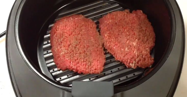 two hamburger patties being cooked in an air fryer