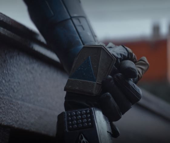 a person wearing gloves and holding a cell phone on top of a wooden roof with buildings in the background