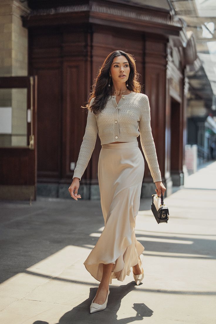 a woman is walking down the street wearing a skirt and sweater with heels on her feet