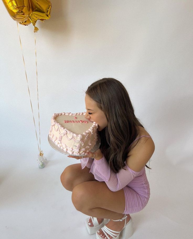 a woman kneeling down with a cake in front of her face