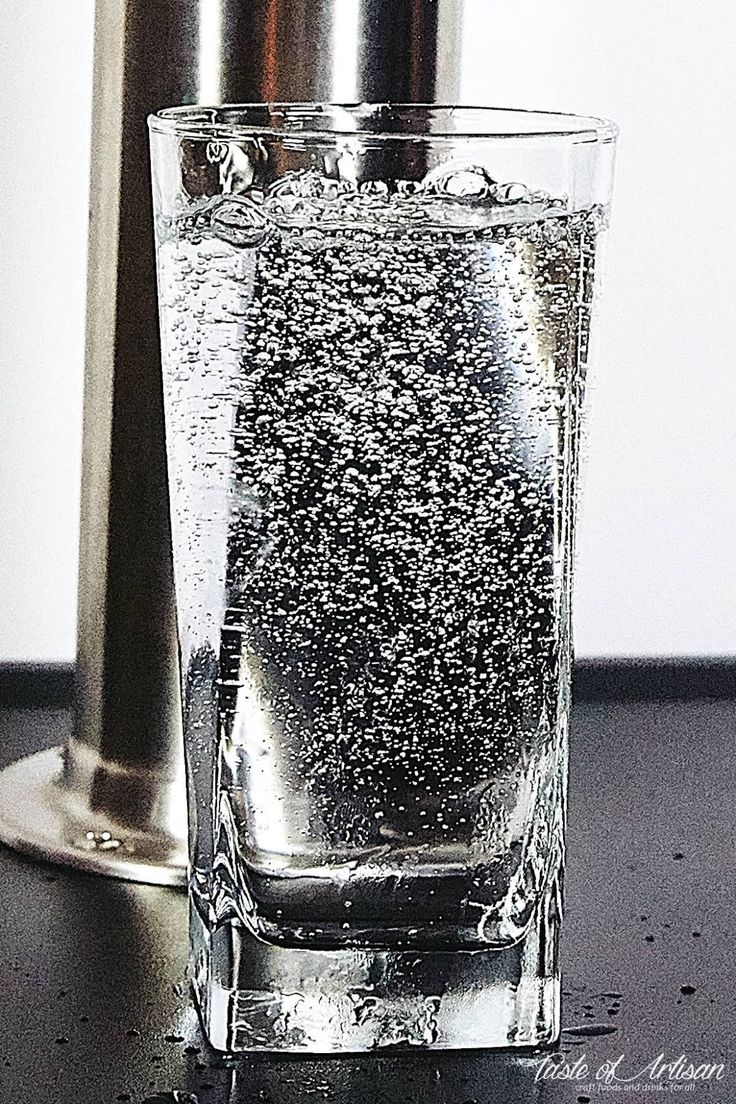 a glass filled with water sitting on top of a table next to a metal faucet