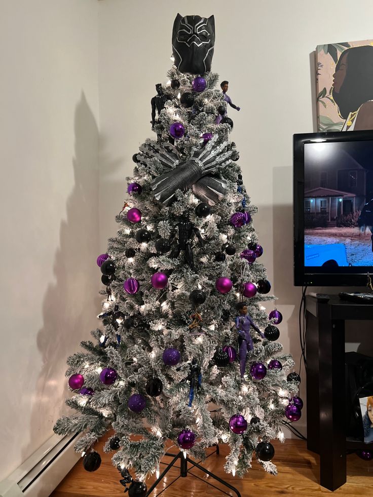 a decorated christmas tree with purple and silver ornaments in front of a television set on a wooden floor