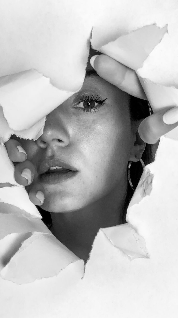 black and white photograph of a woman peeking out from behind the sheets of torn paper