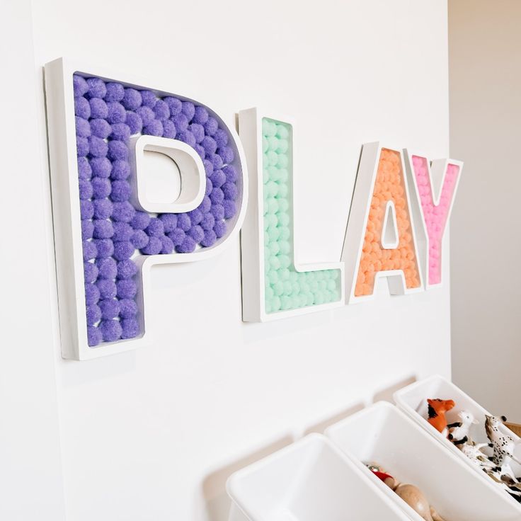 the word play is made out of plastic beads and sits next to a white bin