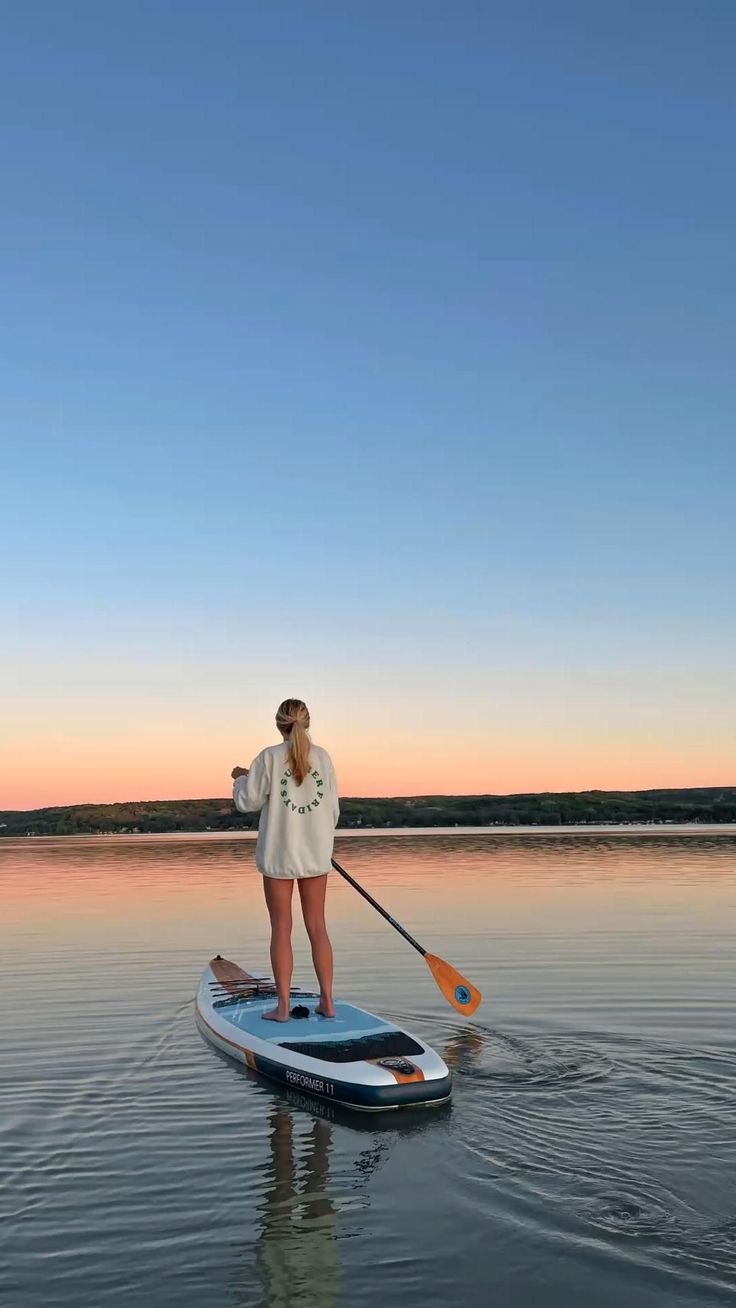 a woman standing on top of a paddle board in the water at sunset or dawn