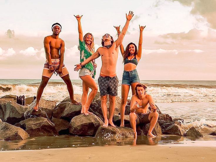 four people standing on rocks at the beach with their arms in the air and hands up