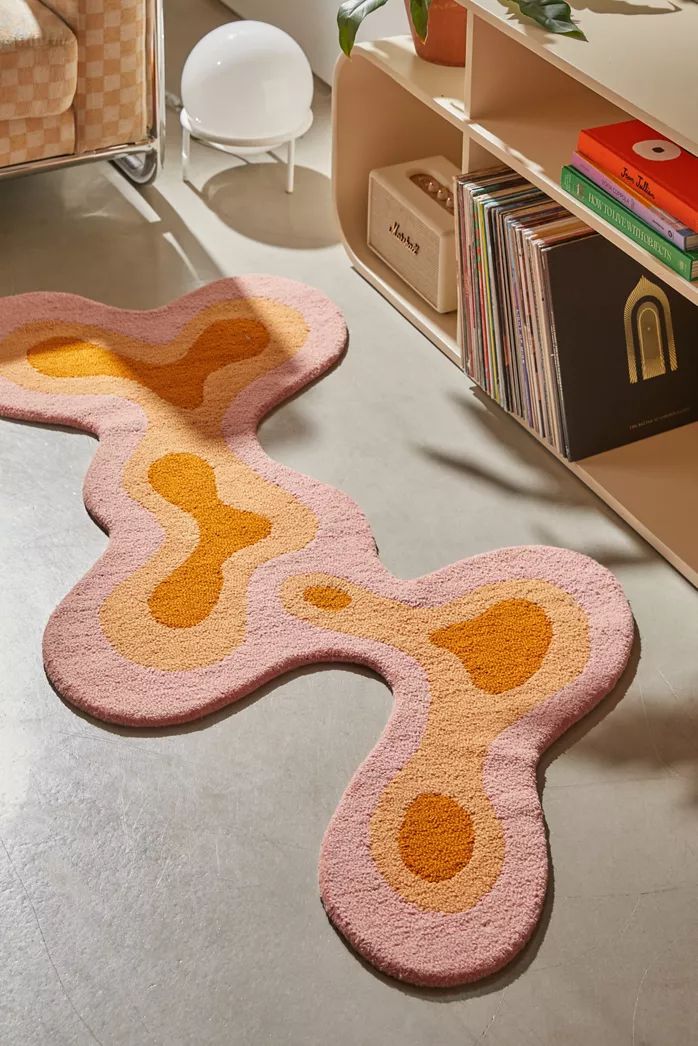 a pink rug with an orange and yellow design on the floor next to a bookshelf