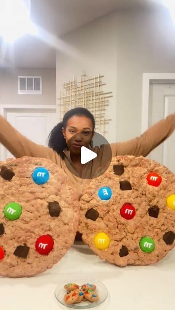 a woman sitting in front of two giant cookies with m & m's on them