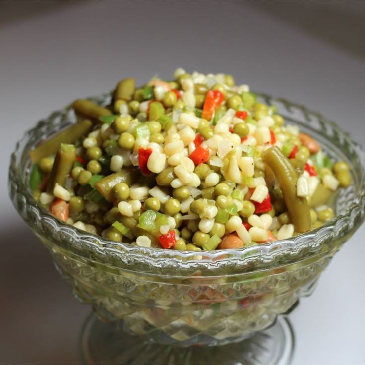 a glass bowl filled with corn salad on top of a white tablecloth covered table