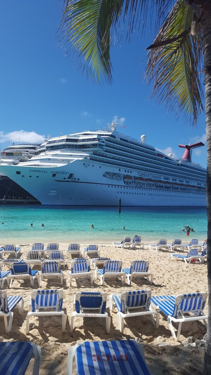 a cruise ship is in the distance as lounge chairs are set up on the beach