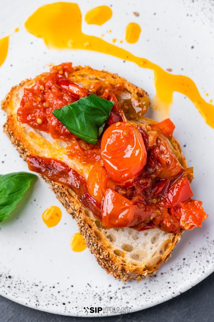 a piece of bread with tomato sauce and basil on it sitting on a white plate