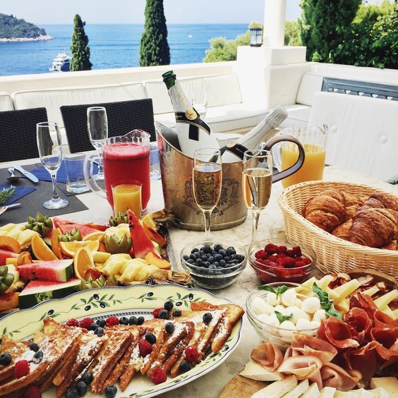 a table full of food and drinks on top of a white table with an ocean view in the background