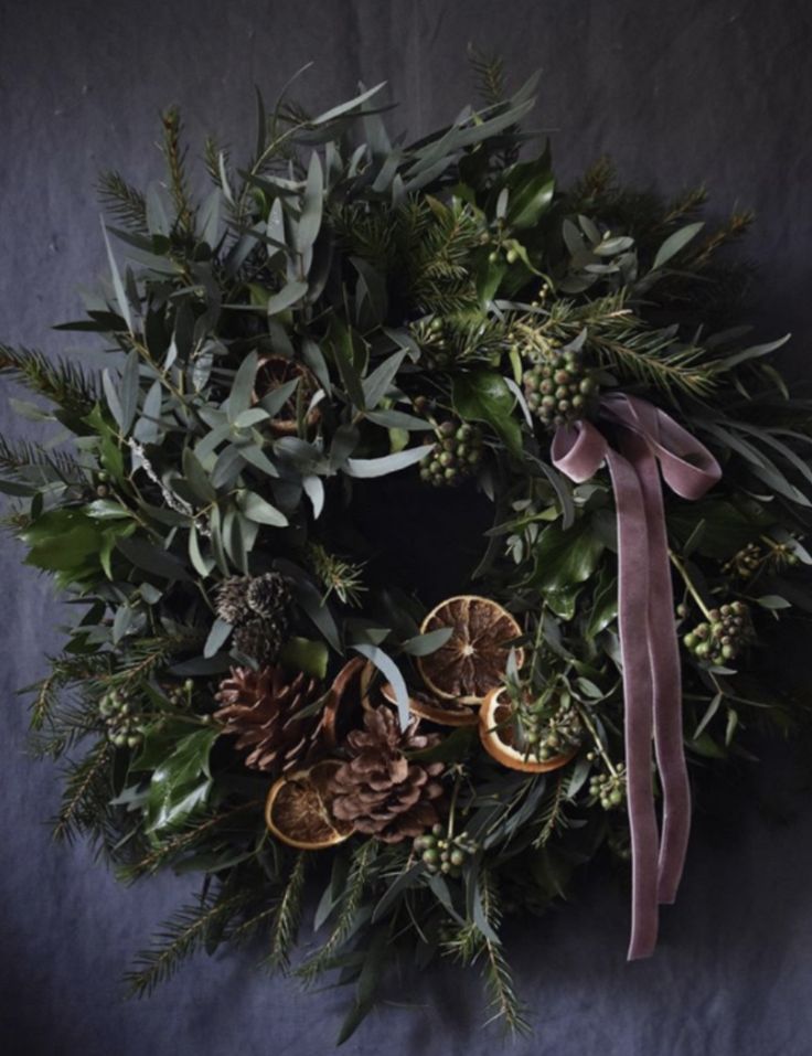 a christmas wreath with pine cones, oranges and greenery on a dark background