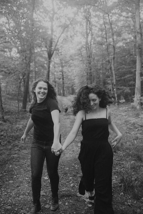 two women walking in the woods holding hands