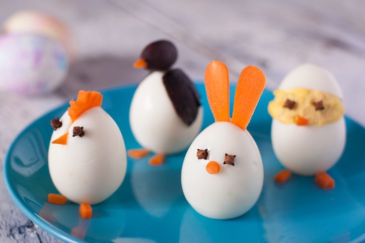 four decorated eggs on a blue plate with an egg in the shape of a chicken