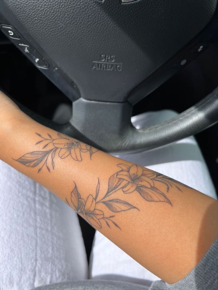 a woman's arm with flowers on it in the passenger seat of a car