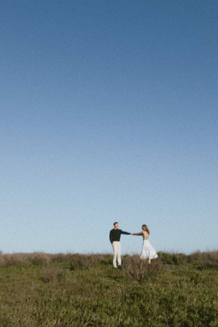 two people holding hands while standing in a grassy field with a kite flying above them