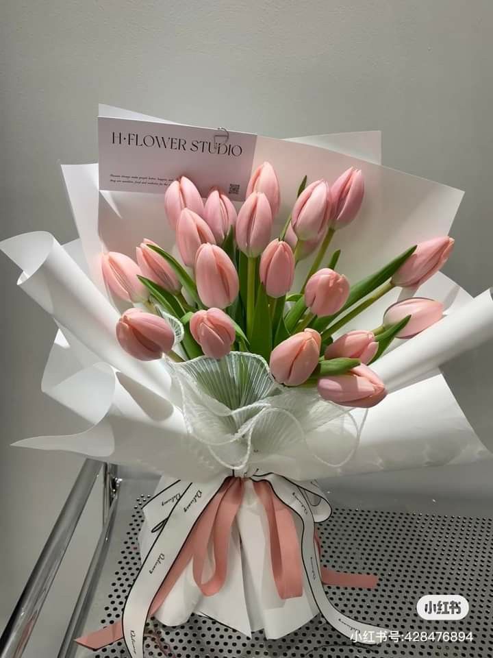 a bouquet of pink tulips is wrapped in white paper and tied with ribbon