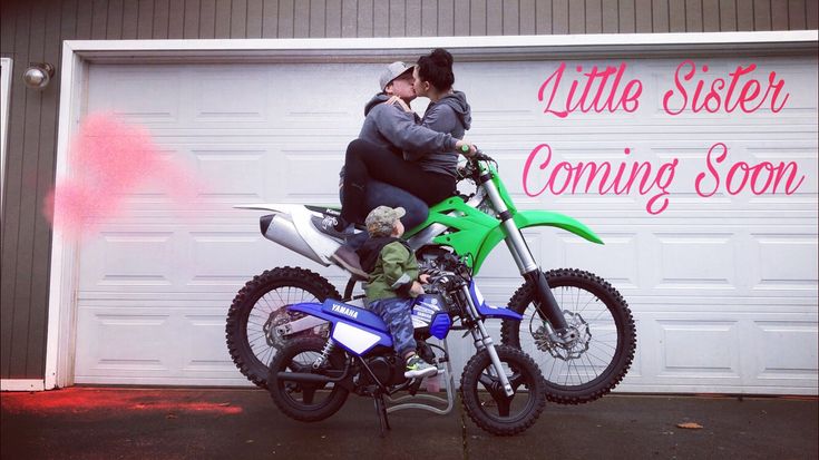 a woman sitting on the back of a green motorcycle next to a man holding a baby