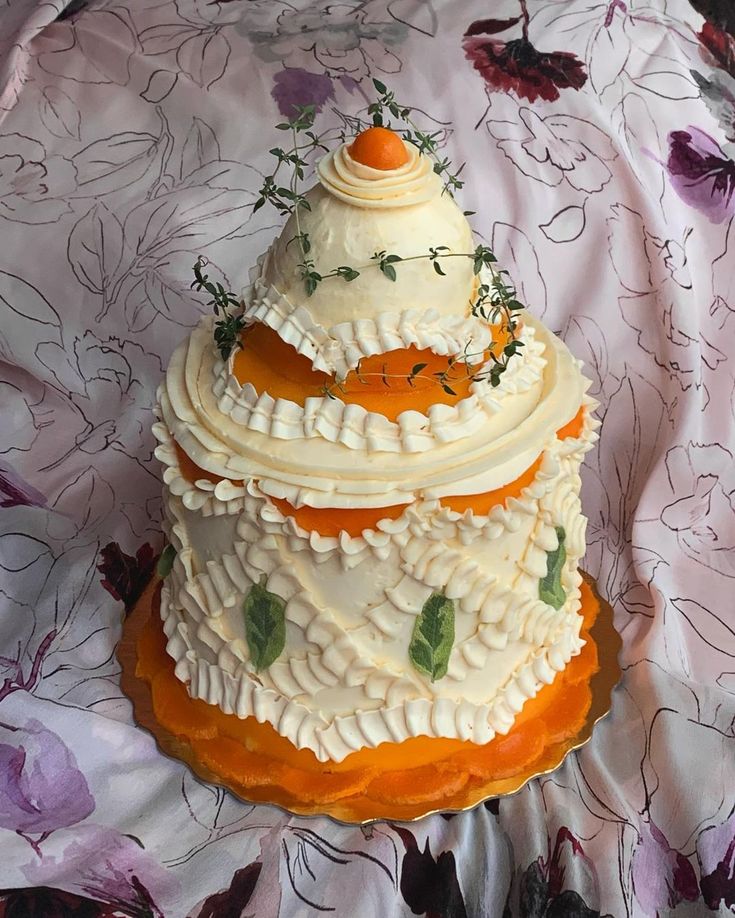 a three tiered cake with white frosting and orange icing on a floral table cloth