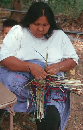 a woman sitting on the ground working with sticks