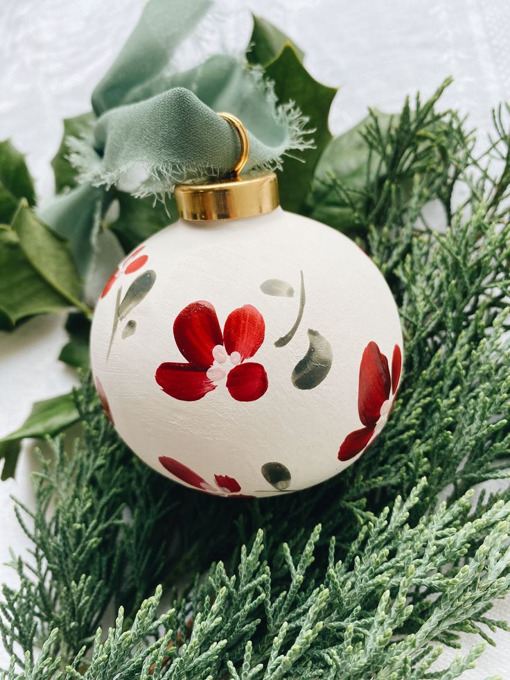 a white ornament with red flowers and green leaves on it's side