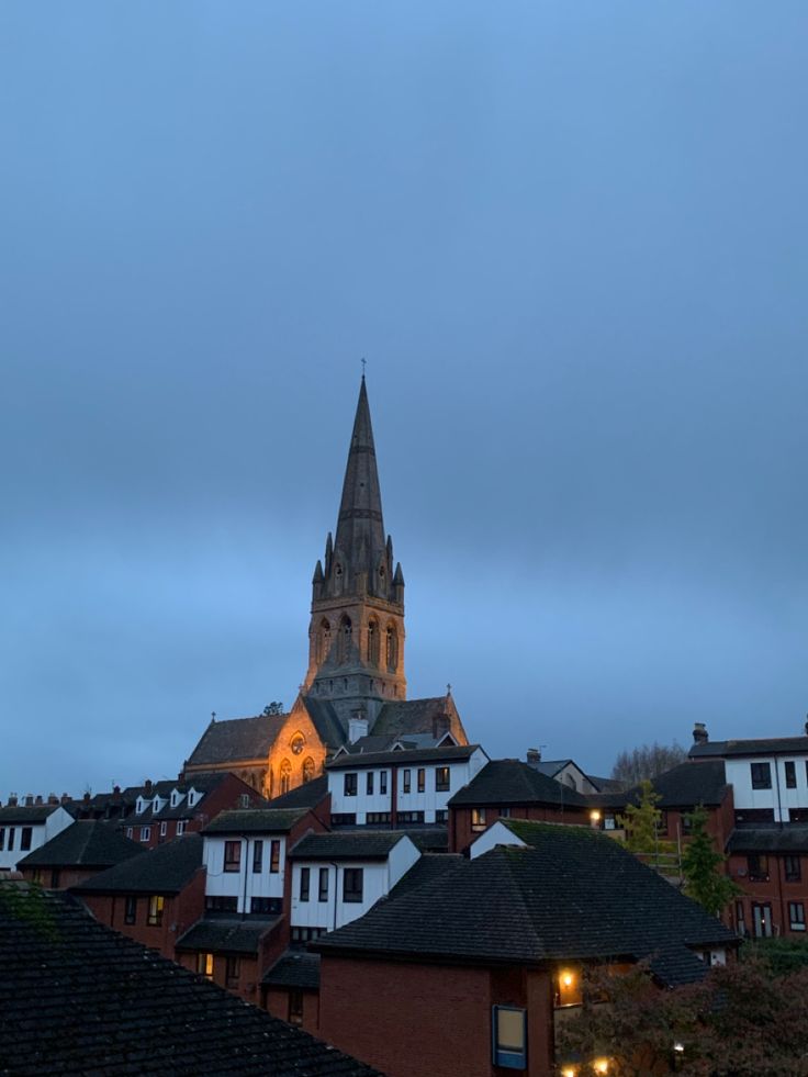 an image of a city at dusk with buildings in the foreground and a church steeple lit up