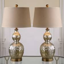 two silver vases sitting on top of a glass table next to a light brown lamp