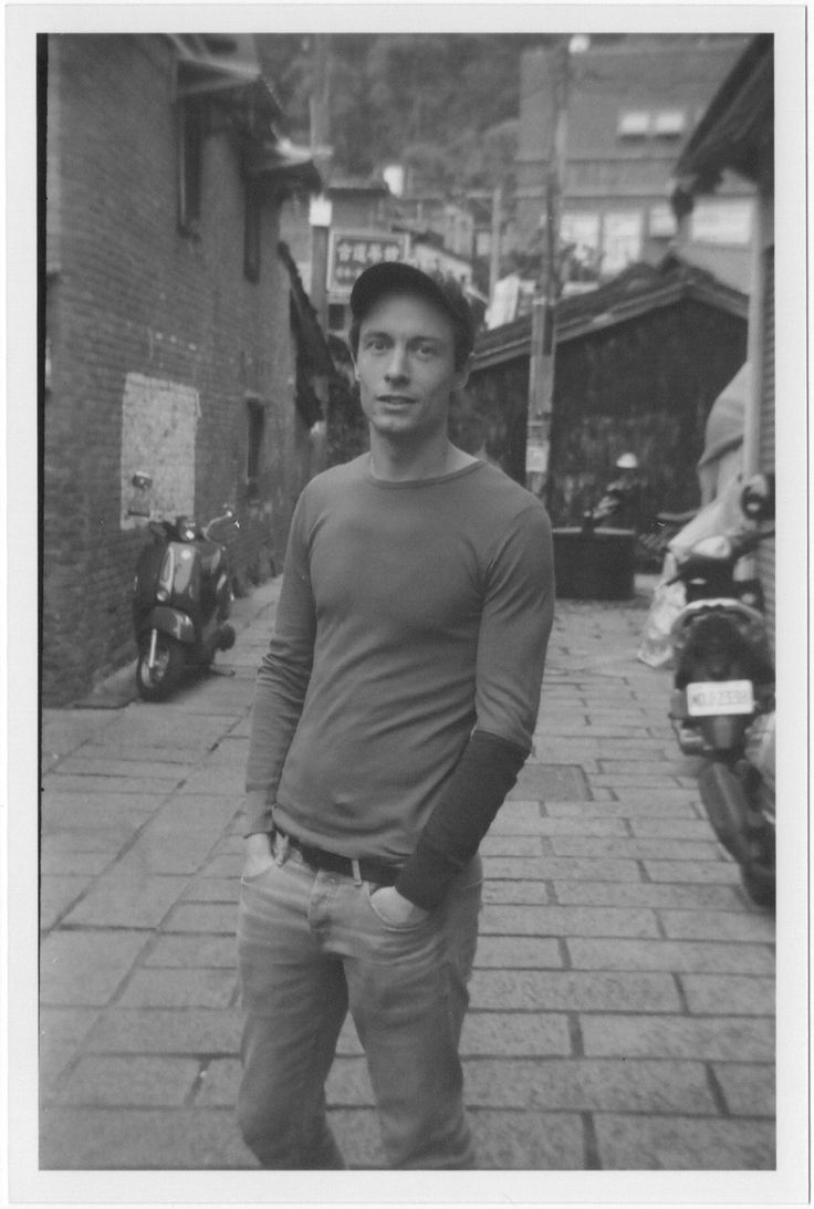 black and white photograph of a man standing in the middle of an alleyway with his hands in his pockets