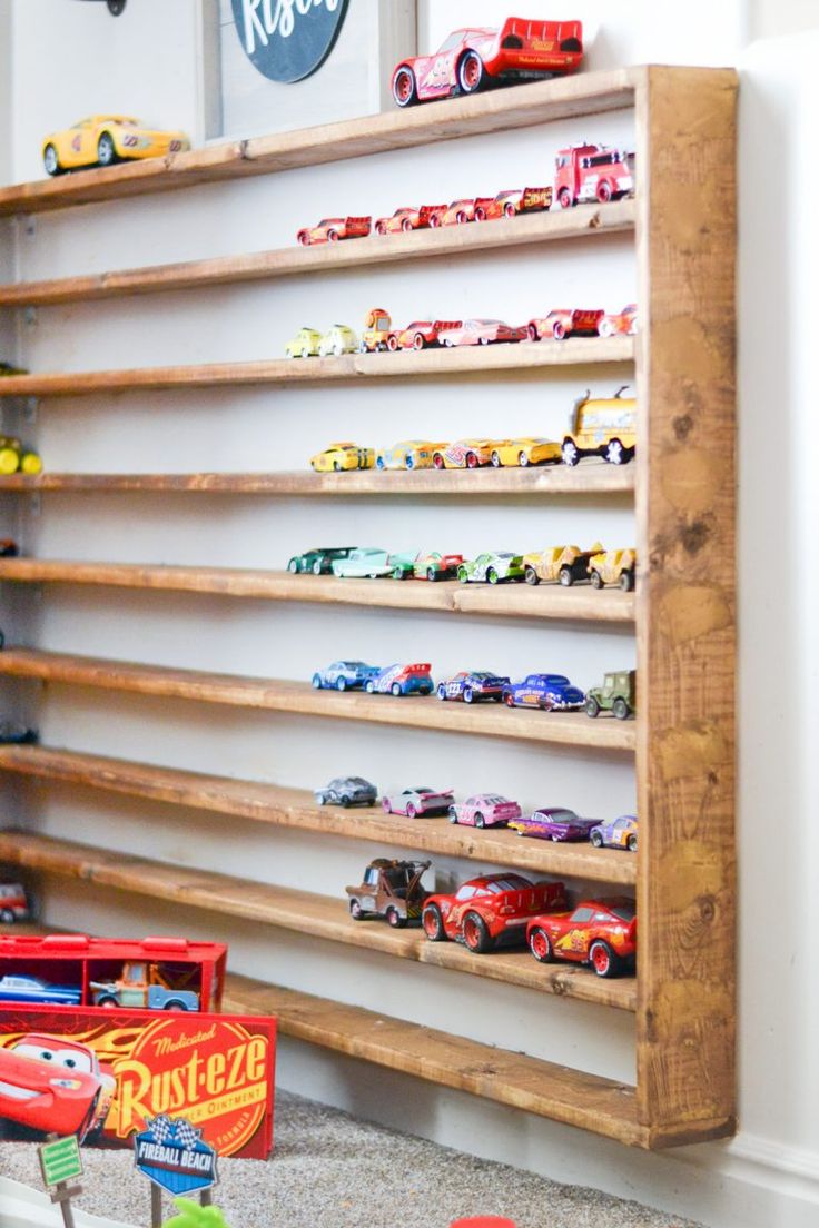 toy cars are lined up on wooden shelves in a playroom with wall hangings