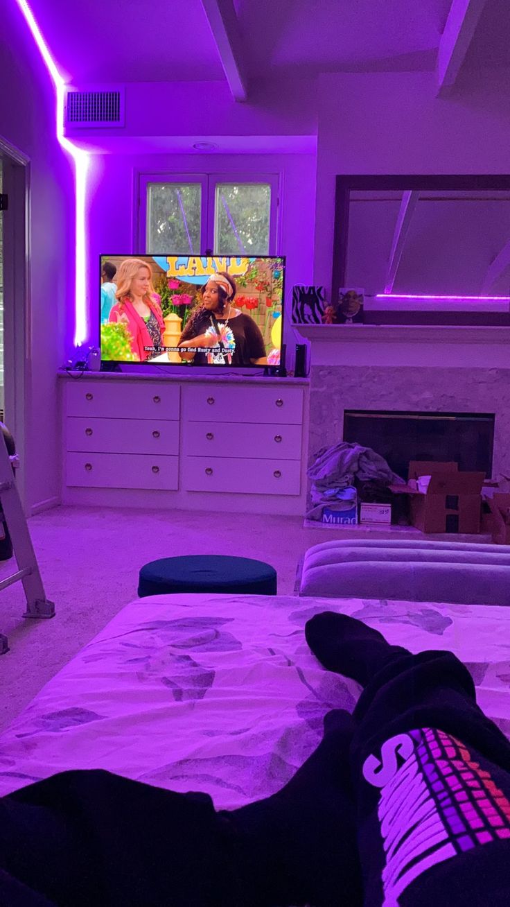 a person laying on a bed in front of a tv with purple lights above them