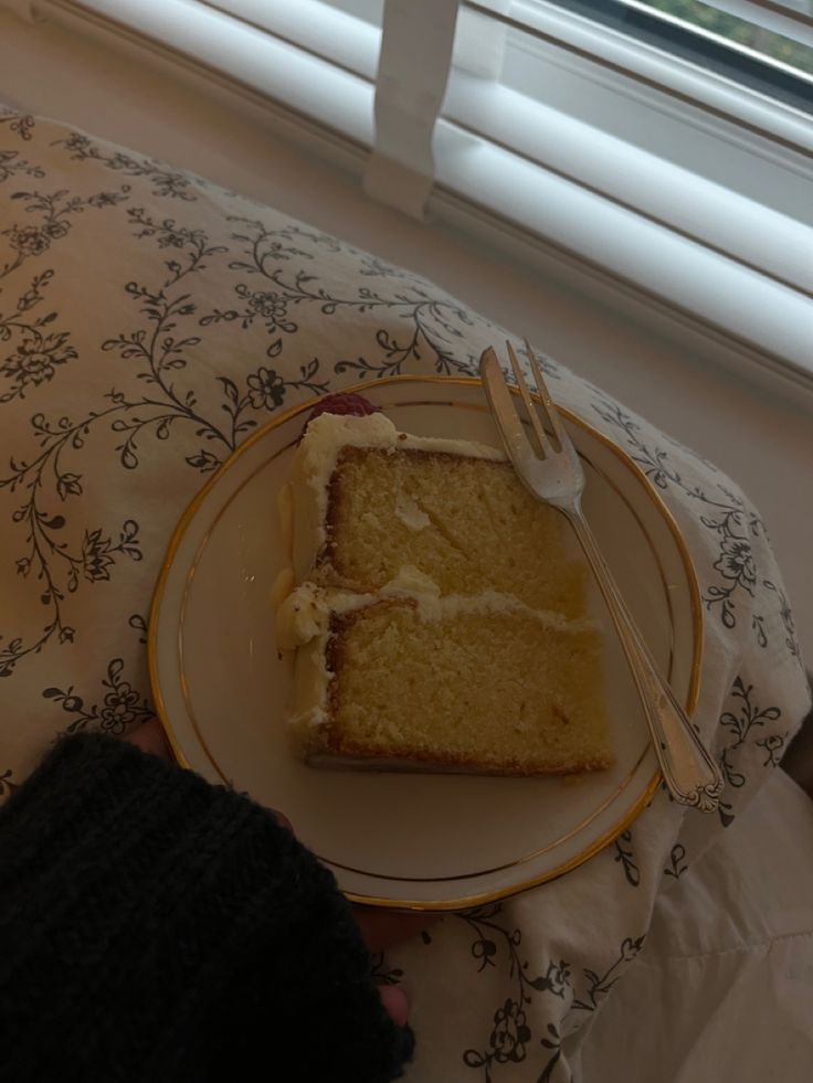 a piece of cake on a plate with a fork in front of it and someone's hand