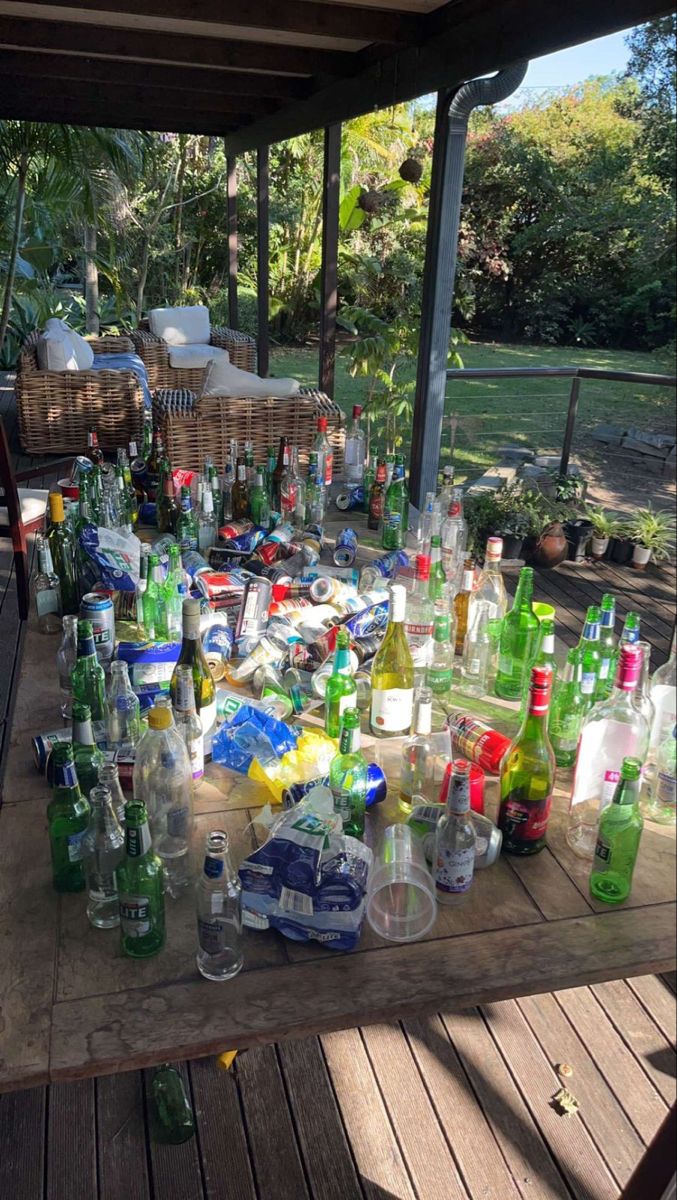 an outdoor table covered in bottles and glasses on top of a wooden deck next to a picnic table