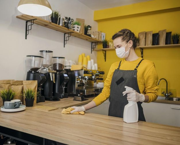 a woman wearing a face mask and gloves is cleaning the counter in a coffee shop