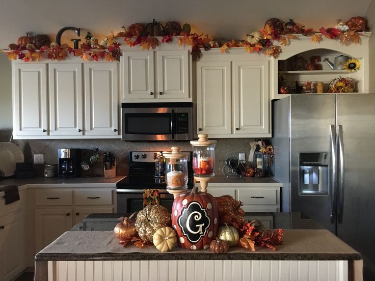 a kitchen filled with lots of white cabinets and counter top covered in fall leaves, pumpkins and candles