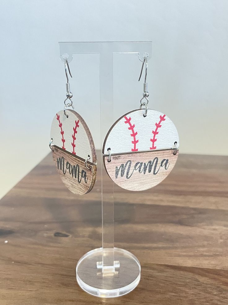 a pair of earrings with baseballs and the word mama on it sitting on top of a wooden table