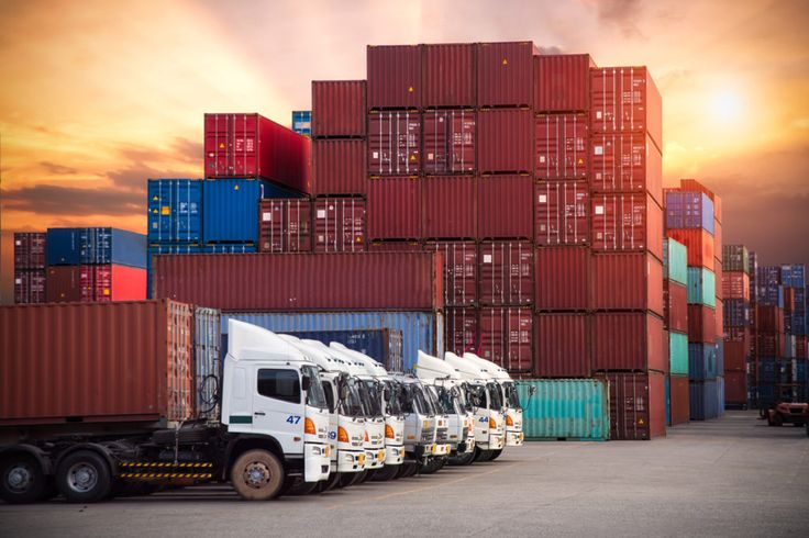 a row of trucks parked next to each other in front of shipping containers at sunset