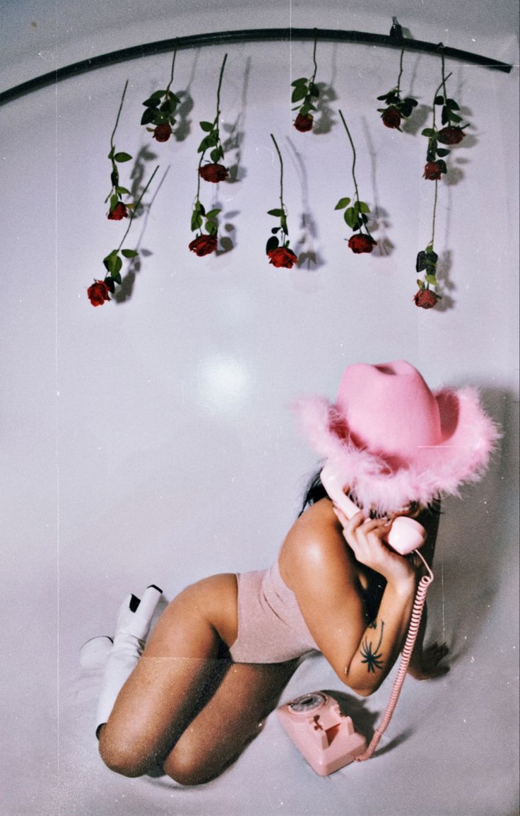 a woman wearing a pink hat and holding a cell phone to her ear while sitting in a bathtub